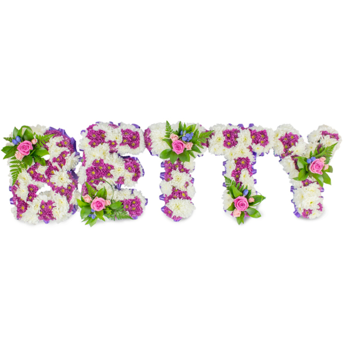 A striking, personalised funeral tribute arranged by Flower Delivery Farnborough, this composition spells the name BETTY in bold, block capitals fashioned from lush white chrysanthemums whose rounded heads form a soft, cloud-like foundation. Within each letter a contrasting band of vibrant purple or magenta chrysanthemums creates an interior pattern and crisp definition, while a slim purple ribbon outlines the sides, adding a finished, tailored edge that complements the floral tones. Carefully placed on several letters - the upper left curve of the B, the cross of the first T and the upper right arm of the Y - are petite bouquets of pale pink roses, some cupped and fragrant, others just beginning to unfurl. Those rose clusters are brightened with small blue flowers, possibly delphiniums or cornflowers, and framed by fern fronds and fresh green sprigs that lend a garden-like softness to the otherwise formal letter shapes. Photographed against a pristine white background and lit softly to reveal texture rather than shadow, the arrangement reads as both elegant and intimate: the powdery white chrysanthemums suggest tranquillity, the purples add dignity, and the pink roses bring a tender, human note. This kind of bespoke name tribute is commonly ordered for funerals and memorial services in Farnborough and neighbouring North Camp and Southwood, where families seek a comforting, hand-crafted expression of love and farewell that is as personal as the name it bears.