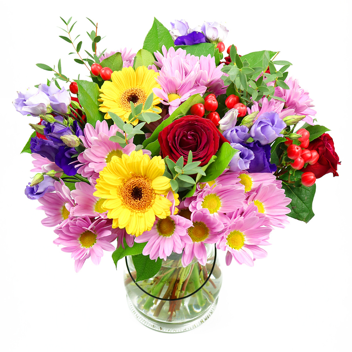 A richly detailed mixed-flower bouquet stands centre stage in a plain clear glass vase, photographed against a bright white background that lets the colours seem almost to glow. At the core of the arrangement, deep red roses spiral open in smooth, velvety layers, their classic shape and intensity of colour giving the design a timeless, romantic anchor. Nestled nearby, two vibrant yellow gerbera daisies with dark, warm-toned centres add a cheerful, almost playful energy, like little suns shining among the blooms. Spreading outwards, generous clusters of soft pink daisies or chrysanthemums provide a gentle halo, their many fine petals and small yellow centres creating a sense of softness and abundance. Woven through this pastel blanket, purple and lavender lisianthus rise in elegant stems, their slightly ruffled, bell-shaped blossoms bringing cool sophistication and a sense of movement. Dotting the arrangement, small rounds of bright red hypericum berries introduce a glossy, tactile accent, reminiscent of berries found on a winter walk through Farnborough's parks. A varied selection of greenery frames everything: broad, darker leaves supply structure, while lighter, more delicate green sprigs give lift and airiness, making the bouquet feel freshly gathered yet expertly shaped. The transparent vase reveals neatly cut stems and clear water, hinting at the care and precision of a trained florist, perhaps preparing the bouquet for a same-day delivery across Farnborough's neighbourhoods. The overall impression is one of joyful celebration and heartfelt thoughtfulness, an ideal arrangement to place on a dining table for a family gathering, offer as a birthday surprise, or simply brighten a quiet corner of a home near Farnborough town centre.