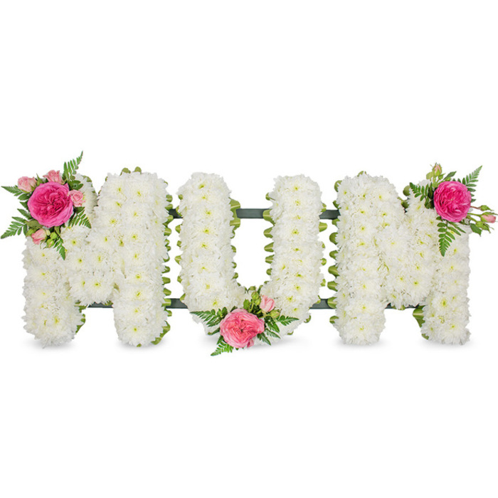 This image shows a lovingly crafted "MUM" funeral flower tribute, photographed straight on against a bright, uncluttered white background so that every detail of the florist's work is easy to imagine. The three capital letters are constructed on a sturdy metal frame, hinted at by glimpses of dark green bars and ribbon along the base, similar to those used by local Farnborough florists for funeral lettering tributes. Each letter is completely and evenly covered with small white spray chrysanthemums, their compact blooms overlapping to form a thick, cushiony texture that appears soft to the touch. The uniform white surface feels calm and dignified, conveying purity, remembrance, and the quiet stillness often associated with a farewell service. To bring gentle colour and individuality, three coordinated clusters of pink flowers and foliage have been added as decorative accents. The first cluster, placed on the upper left arm of the first "M", features a striking fuchsia-coloured rose surrounded by lighter pink spray roses and partly opened buds, all nestled into the white chrysanthemum base. Finely cut green fern fronds extend outwards, adding movement and a natural, feathery rhythm. A second cluster, mirroring the first, sits low in the curve of the central "U", drawing the eye toward the centre of the word. The third cluster crowns the upper right side of the final "M", completing a visually balanced triangle of colour. The overall design feels both traditional and deeply personal, the kind of floral lettering tribute often chosen in Farnborough to rest beside the coffin or on the graveside, offering a final, beautifully fragrant message of enduring love and gratitude to Mum.