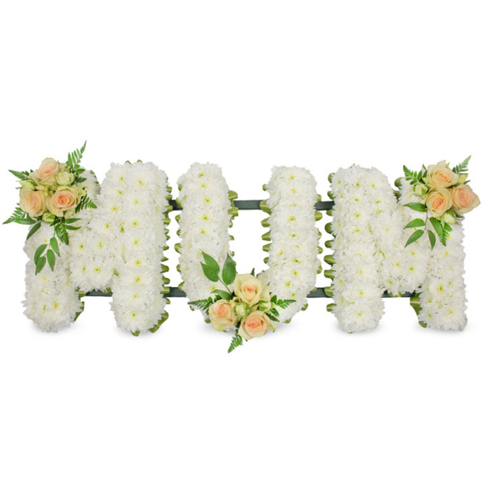 This poignant floral arrangement presents the word MUM in large, upright capital letters, arranged in a long horizontal line as if resting on a low stand in a Farnborough funeral chapel, yet photographed against a bright white background so that only the flowers and their structure are visible. Every letter is completely clad in white spray chrysanthemums, their small, star-like blooms layered tightly together to give a plush, uniform surface that looks both soft and enduring. The chrysanthemums' pure white tone conveys innocence and remembrance, with each tiny floret adding to the sense of abundance and care. A narrow dark green frame or ribbon outlines the letters, occasionally glimpsed between petals and at the outer edges, hinting at the skilled floristry work that holds the design firmly in place for the journey to the service. Three groupings of roses in gentle shades of peach, blush pink, and cream bring warmth to the tribute. One cluster sits at the top left shoulder of the first M, another rests at the lower centre curve of the U, and the last is positioned on the top right shoulder of the final M, creating a visually balanced triangle of colour. Each cluster combines open roses, half-open blooms, and buds, edged with glossy darker leaves and airy fern-like fronds that arc softly over the chrysanthemums. The overall effect is tender and composed, with a quiet beauty that feels suitable for a memorial in Farnborough, whether at a local church or crematorium. It reads as a final, loving thank-you to a mother, carrying thoughts of shared Sunday walks, family gatherings, and the everyday warmth she brought to her home and community.