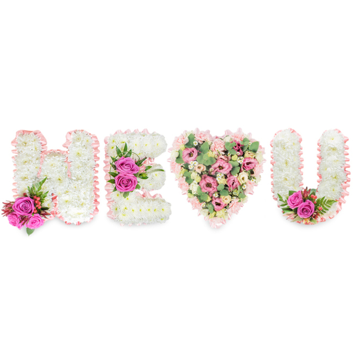 This elegant tribute, photographed against a stark white background, spells H, E, a heart and U from left to right, each character crafted to speak with tactile clarity and quiet emotion. The H and E are constructed from dense beds of snowy white chrysanthemums whose tiny petals form a velvety, even surface; both letters are neatly edged in a soft blush-pink satin ribbon that reads like a ribboned note of condolence. The H is softened at its base by an accent of two vibrant fuchsia roses, intermingled with small clusters of reddish-pink berries and slender, almost feathery deep-green foliage that adds movement and contrast. Similarly, the E carries a larger flourish of three fuchsia roses along its central bar, the rich pinks pulling the eye into the middle of the composition. Where a simple stroke might appear, a generous heart replaces it, layered with pale pink carnations and blush lisianthus or small roses, dotted with pale green eucalyptus leaves that create cooling, silvery highlights and a faint, comforting scent. The heart's blush-ribbon outline ties it to the letters, completing a cohesive visual sentence. The U rounds the arrangement in white chrysanthemums, trimmed with ribbon and punctuated at its inner lower curve by two fuchsia roses and deeper green foliage. Bathed in gentle light that emphasizes texture and colour, this arrangement evokes both tenderness and dignity-equally fitting for an intimate funeral service in Farnborough or as a loving display for a quiet anniversary remembrance.